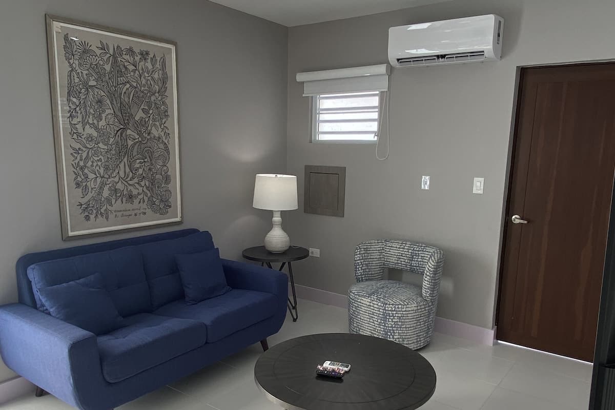A modern living room with a blue sofa, a round coffee table, a patterned armchair, a floor lamp, and a large abstract painting on the wall.