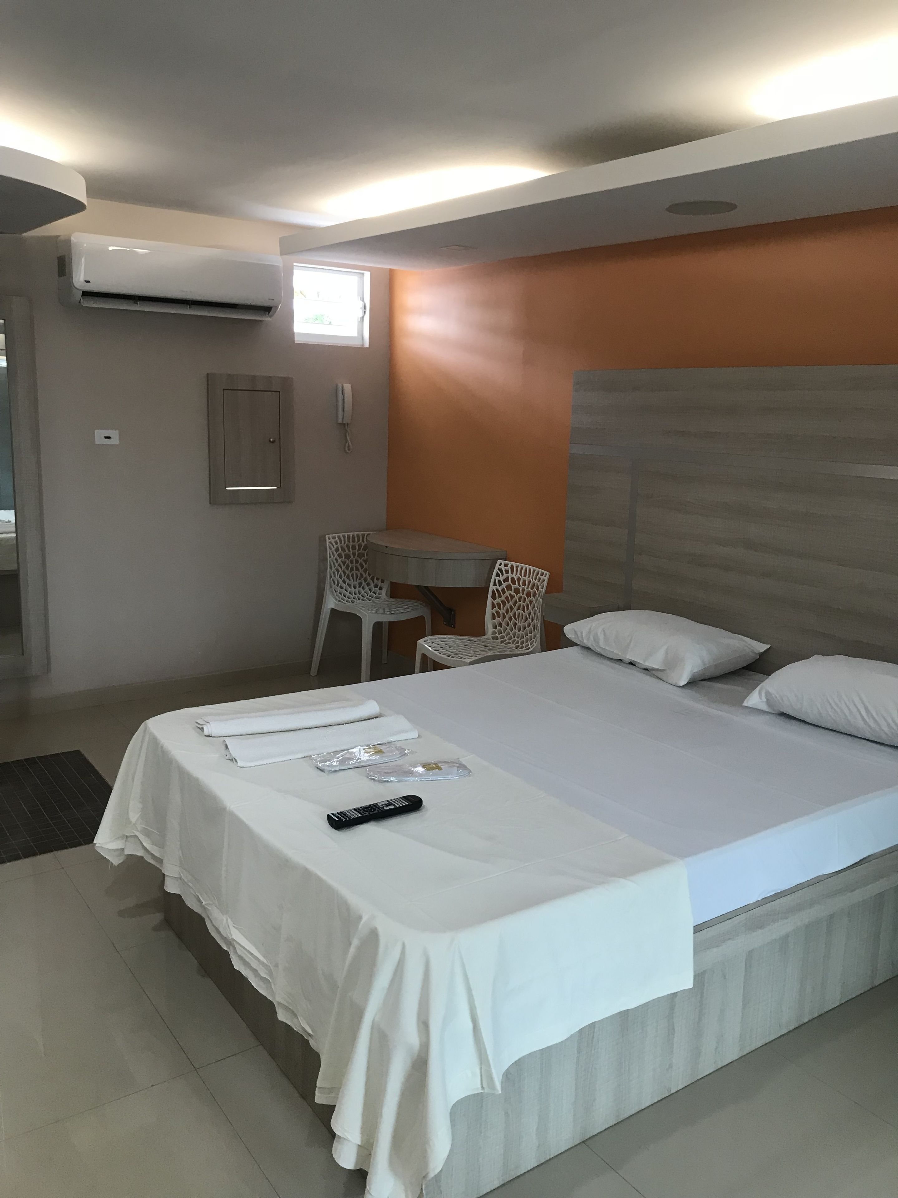 Een hotelkamer met een groot bed, een klein tafeltje, twee stoelen, een airconditioning en een telefoon aan de muur.