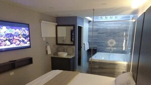A modern hotel room with a bed, a TV, a bathroom with a shower, and a small sink. - Hotel Nuevo Mejico (Ponce)