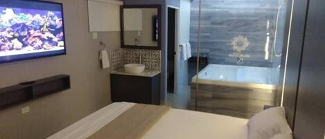 Ein modernes Hotelzimmer mit Bett, Fernseher, Badezimmer mit Dusche und einem kleinen Waschbecken.