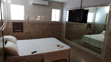 A hotel room with a bed, a TV, a shower area, and a mirror.