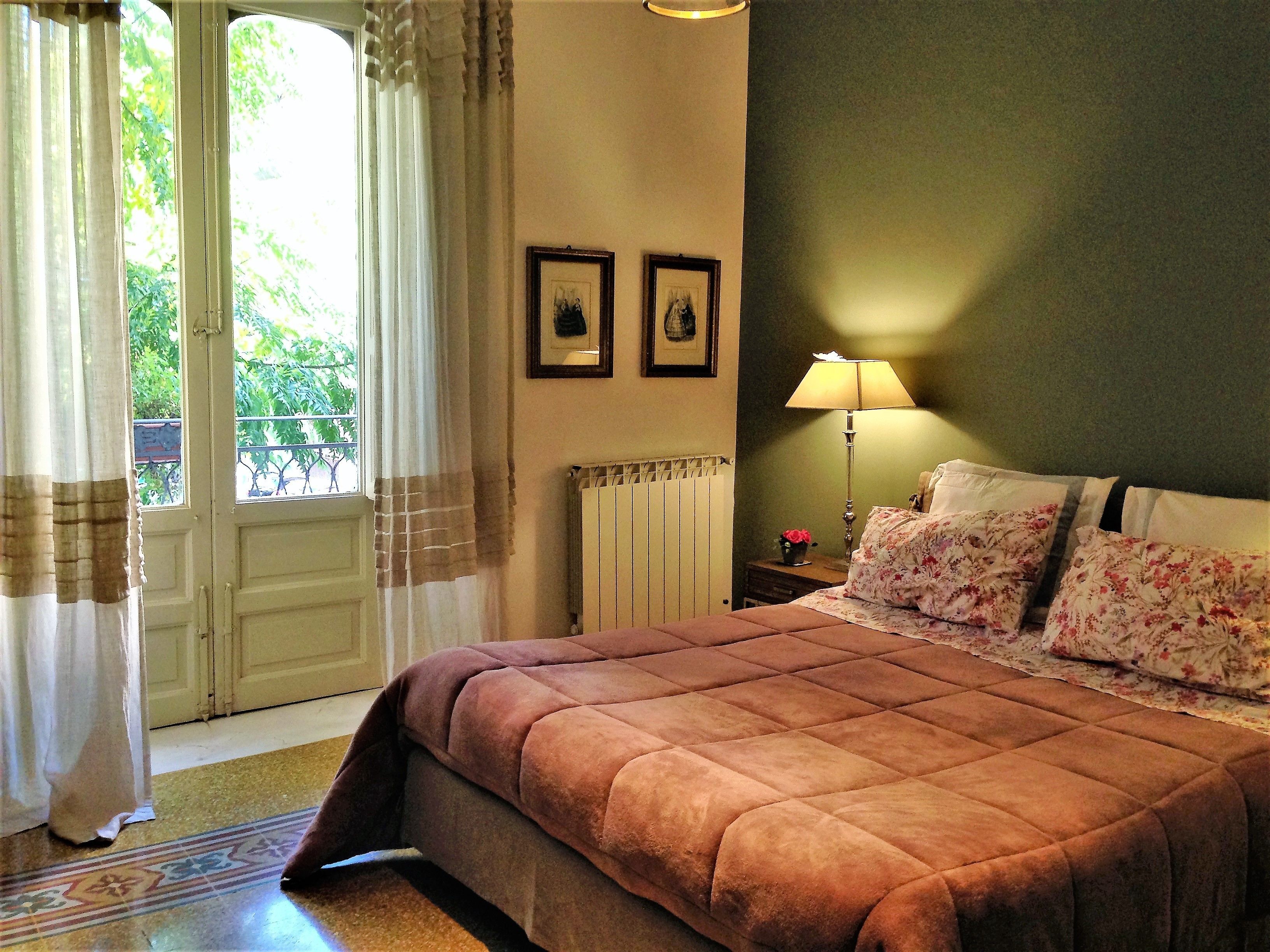 Un dormitorio con una cama grande, una mesita de noche con lámpara, un radiador y dos cuadros en la pared.