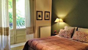 A bedroom with a large bed, a nightstand with a lamp, a radiator, and two framed pictures on the wall. - A Casa di Amelie (Palermo)