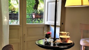 A room with a view of greenery outside, a table with a lamp, a chair, and a patterned floor. - A Casa di Amelie (Palermo)