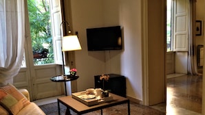 A living room with a sofa, a coffee table, a lamp, a TV, and a small table with flowers. - A Casa di Amelie (Palermo)