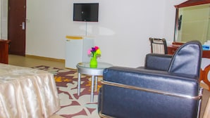 A hotel room with a bed, a chair, a small table with a vase, a television on the wall, and a mirror. - New Rivoli Hotel Benin (Cotonou)