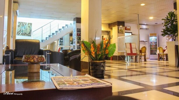 A hotel lobby with a reception desk, seating area, and a staircase in the background. - New Rivoli Hotel Benin (Cotonou)
