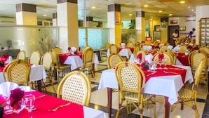 A restaurant with multiple tables set with red tablecloths and gold chairs. - New Rivoli Hotel Benin (Cotonou)