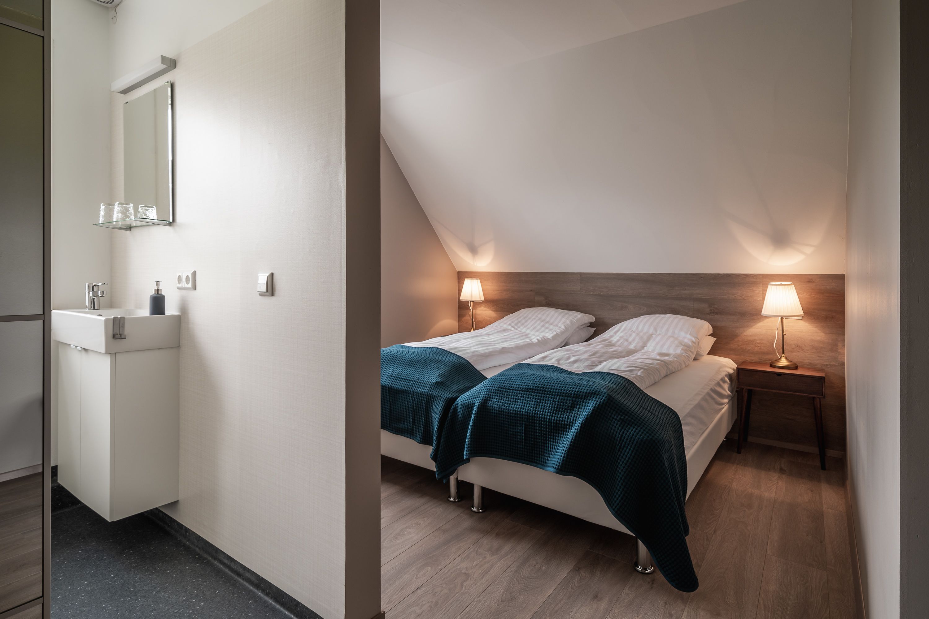 A bedroom with a bed, bedside lamps, a nightstand, and a wooden headboard.