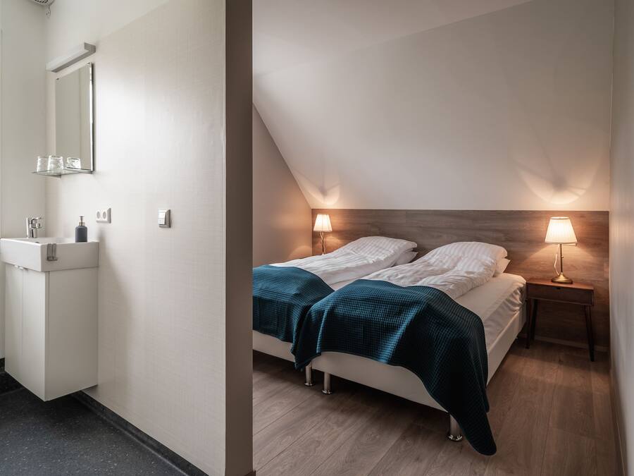 A bedroom with a bed, bedside lamps, a nightstand, and a wooden headboard.