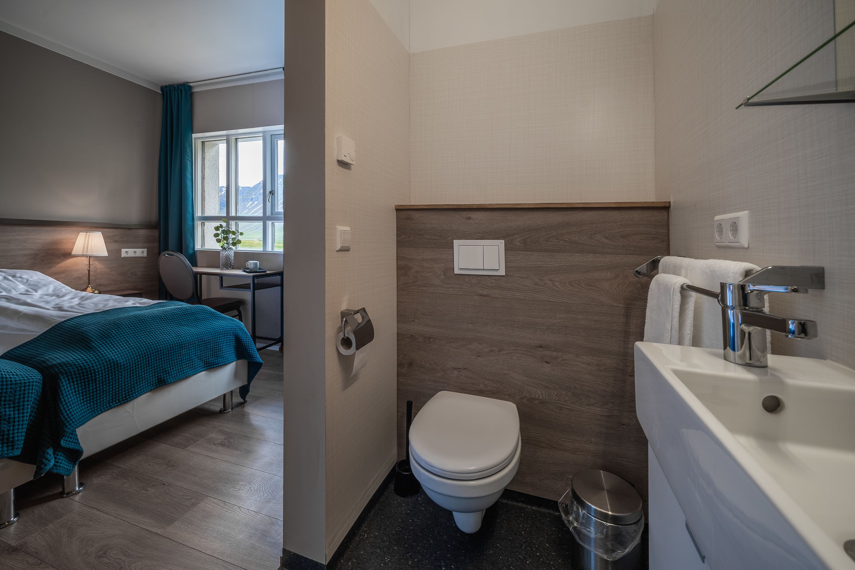 Ein Hotelzimmer mit Bett, Schreibtisch mit Lampe, Toilette und Waschbecken.