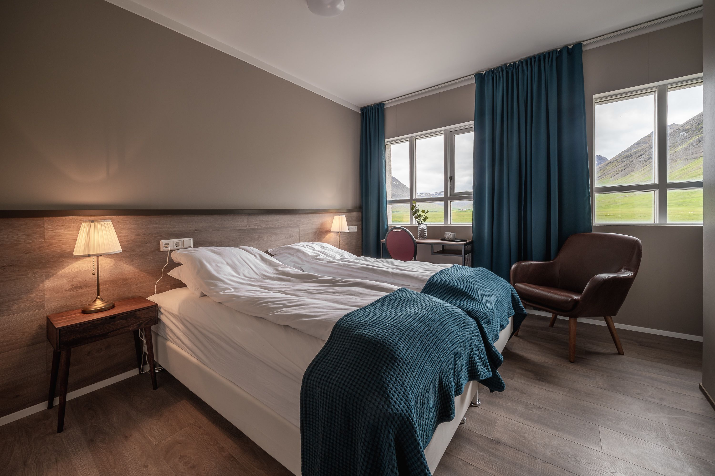 A hotel room with a bed, bedside lamp, chair, and a view of the outdoors.