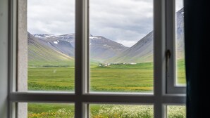 A view through a window of a green field, a small house, and mountains with snow. - Holt Inn (Holt)