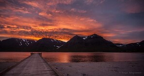 A wooden pier extending into a calm lake with mountains in the background and a sunset sky.