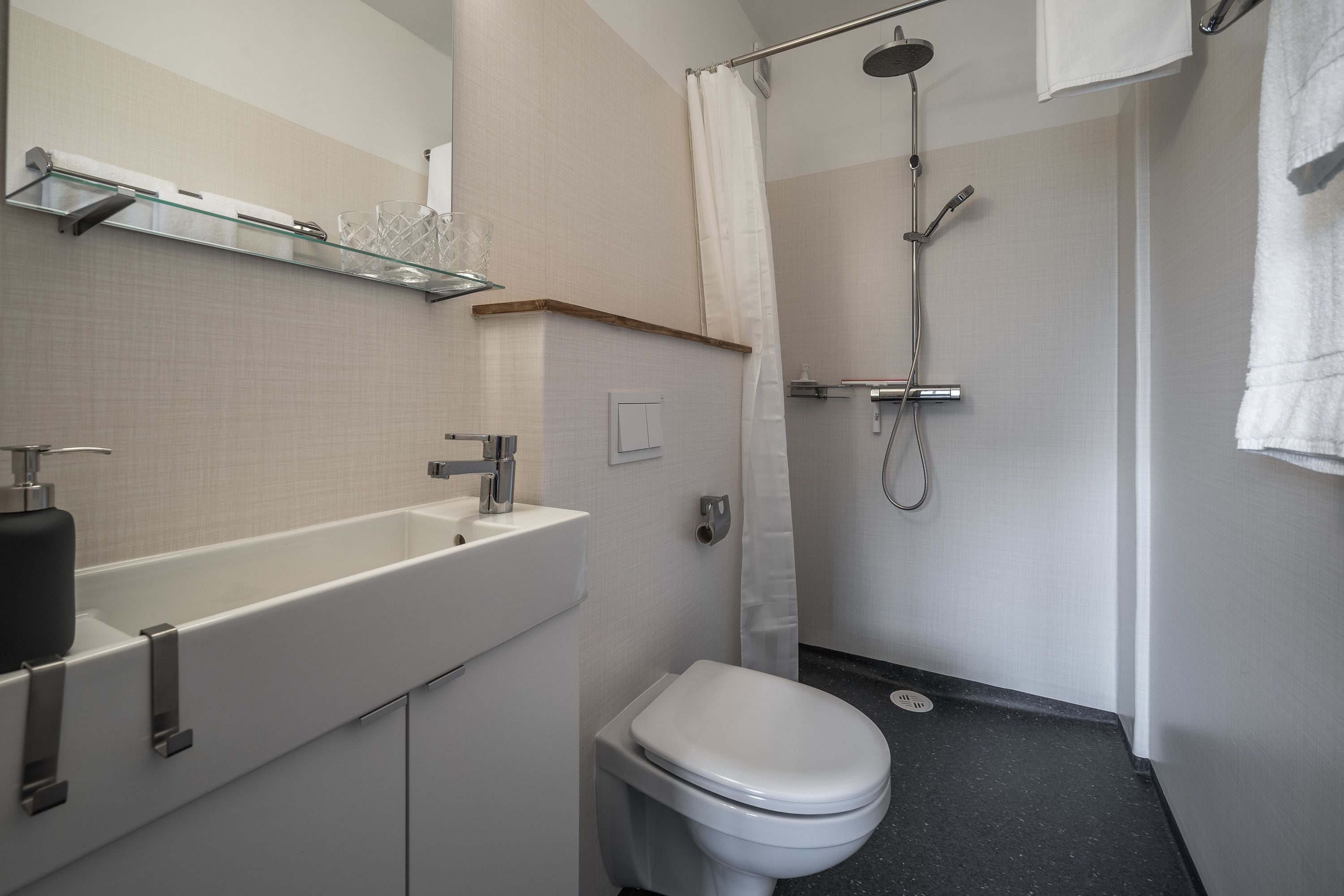 A modern bathroom with a glass shelf, white sink, and toilet.