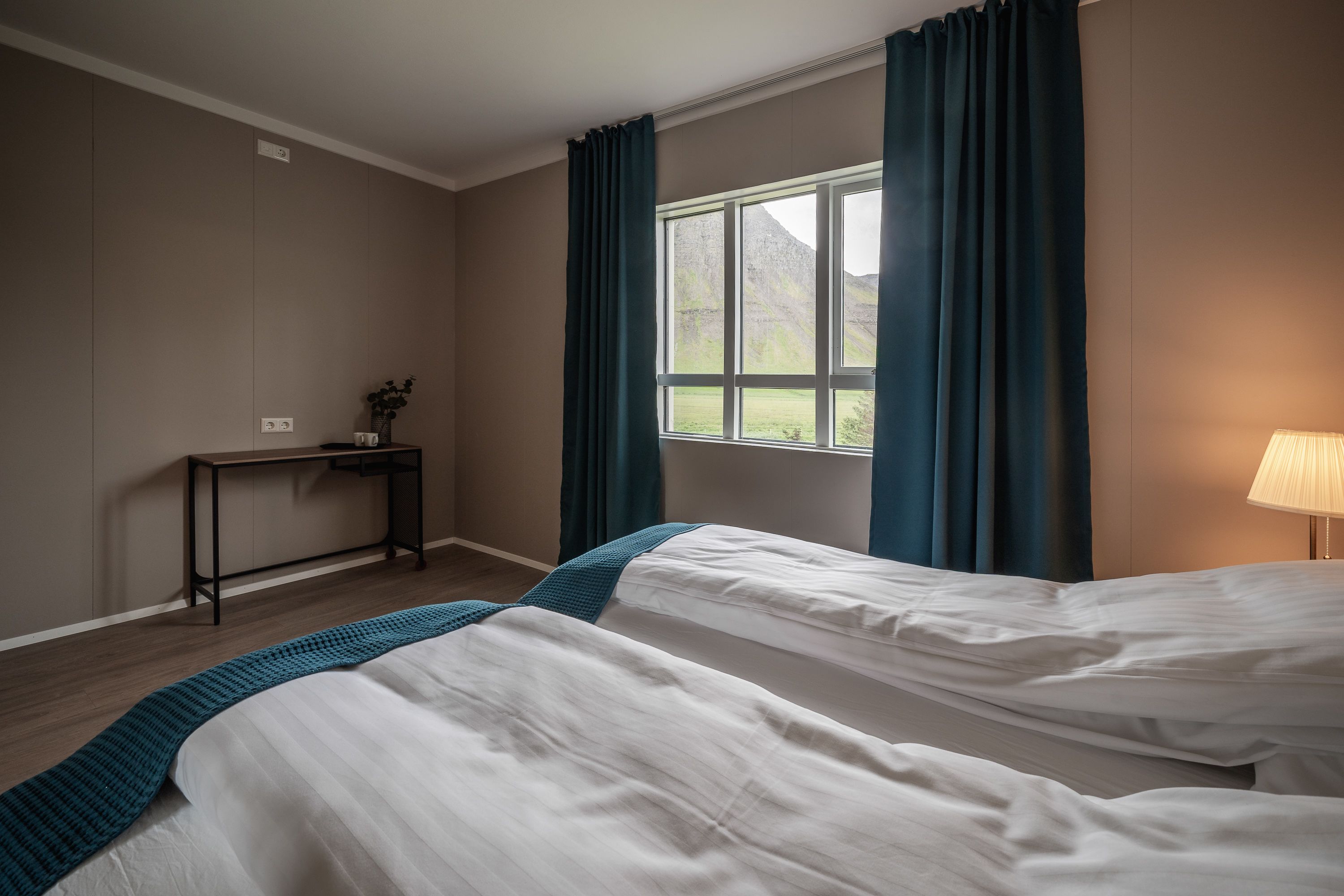 Un dormitorio con dos camas, un escritorio, una lámpara y una ventana con cortinas.
