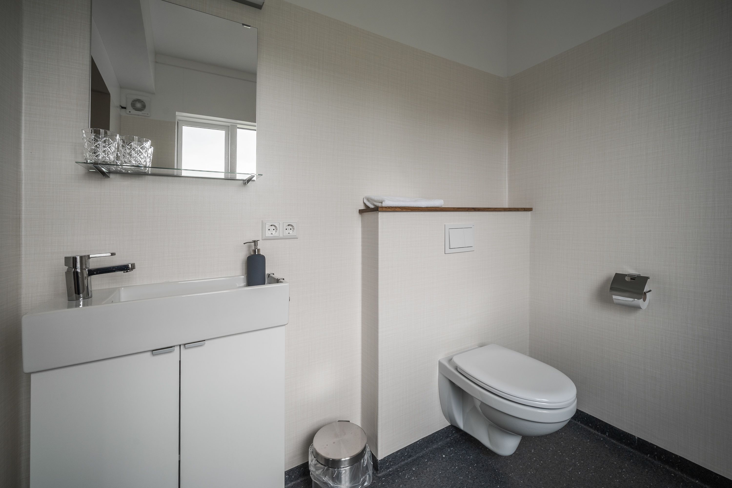 A modern bathroom with a white sink, mirror, and toilet.