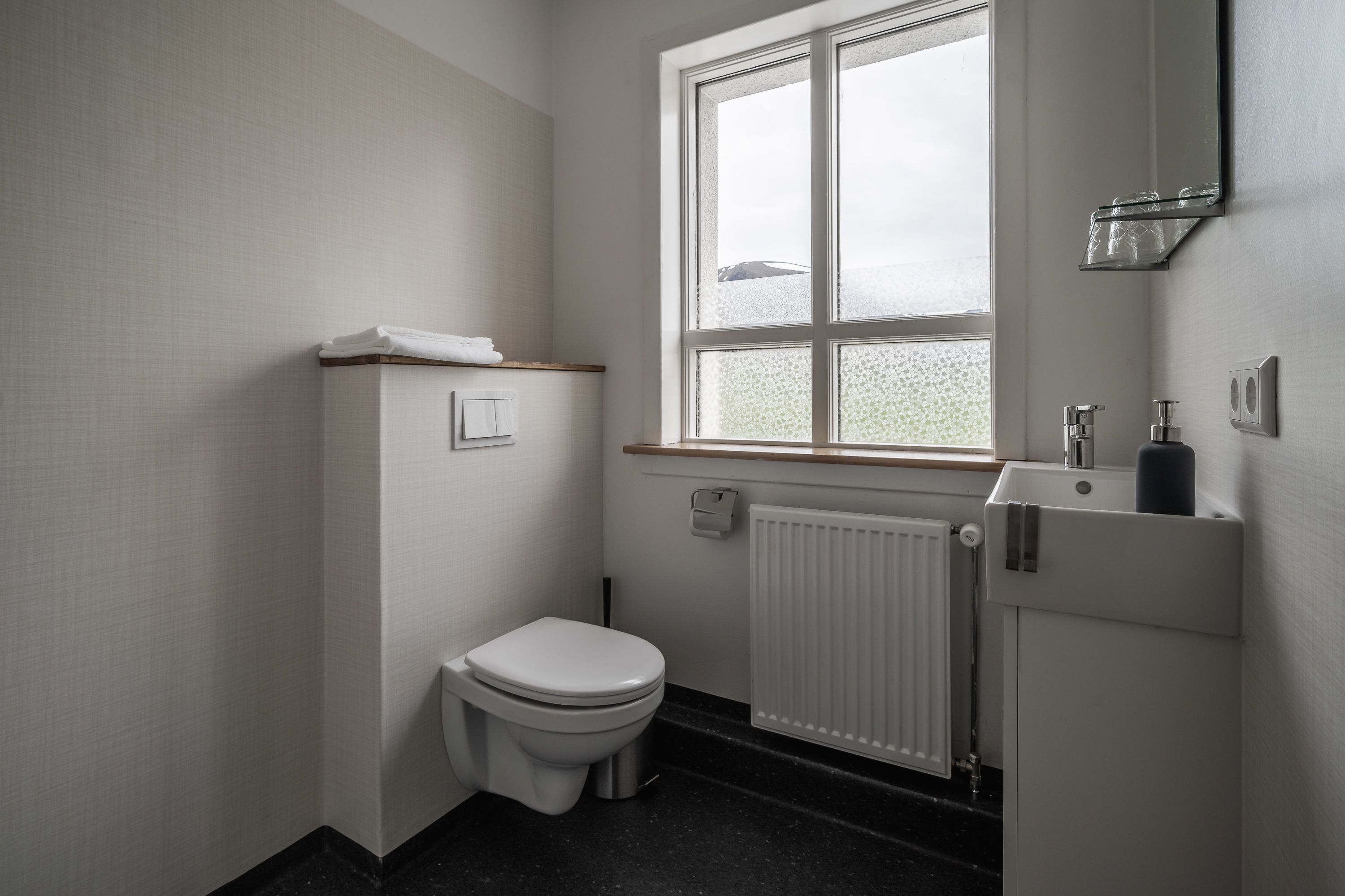 A small, clean bathroom with a toilet, a window, and a radiator.