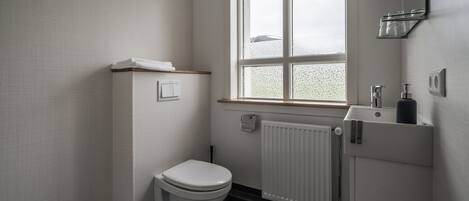 A small, clean bathroom with a toilet, a window, and a radiator.