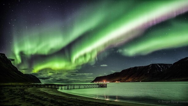 A pier extending into a calm body of water with a backdrop of mountains and the Northern Lights. - Holt Inn (Holt)