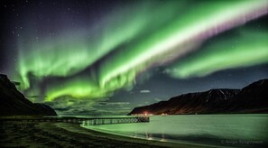 A pier extending into a calm body of water with a backdrop of mountains and the Northern Lights. - Holt Inn (Holt)