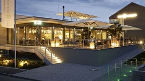 An outdoor restaurant with tables and umbrellas, a staircase, and a building with a sign in the background.