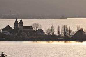 A riverside town with historic buildings, including a church with two towers, and a calm water body reflecting the structures.