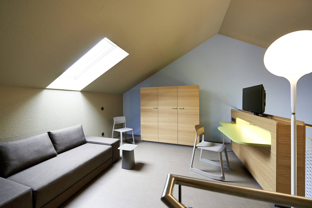 Una habitación moderna y bien iluminada con sofá, sillas, escritorio y armario.