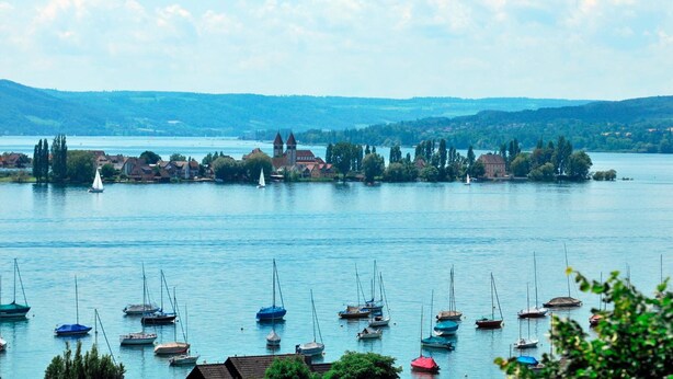A calm lake with boats and houses in the background.