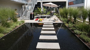 A modern outdoor area with a water feature, steps leading to a seating area, and a staircase to an upper level.