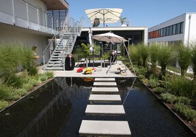 Un espacio exterior moderno con una fuente de agua, escalones que conducen a una zona de estar y una escalera a un nivel superior.