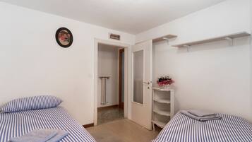 Habitació amb dos llits, un radiador, una porta que dona al bany i una estant amb un ram de flors.