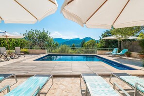 A swimming pool with lounge chairs and umbrellas, surrounded by greenery and mountains. - Country House "Coster" in a Quiet Location with Pool (POLLENSA)