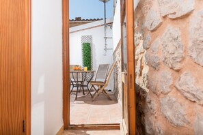 Une porte ouverte donne sur un patio où se trouvent une table et des chaises, une plante verte et un mur en pierre.