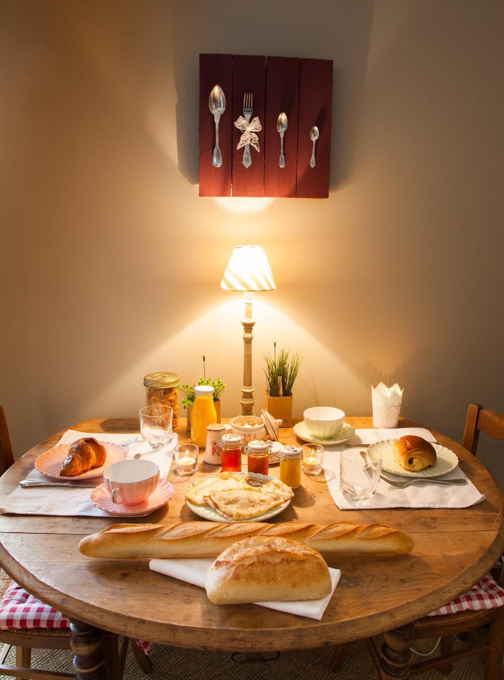 Une table de salle à manger en bois, sur laquelle sont disposés divers aliments pour le petit-déjeuner, notamment des croissants, du pain et une lampe.