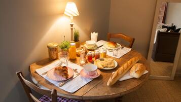 A wooden dining table with a lamp, various food items, and a chair with a checkered cushion.