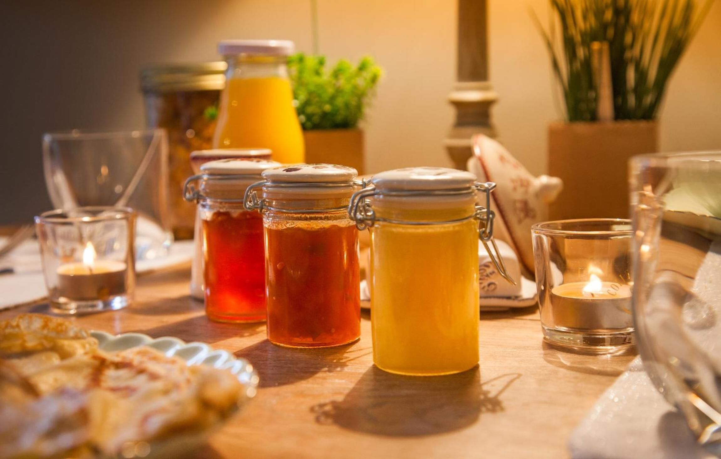 A breakfast table with jars of preserves, a candle, and a glass of orange juice.