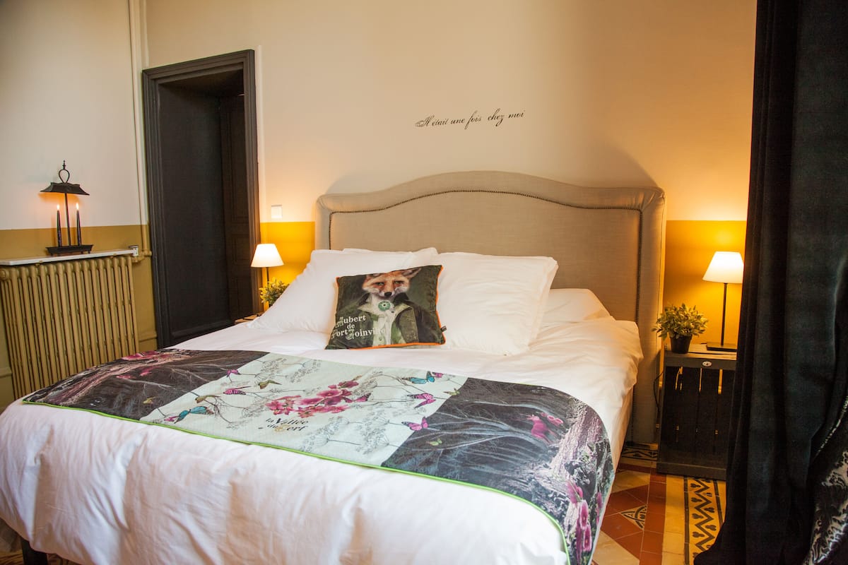 A neatly made bed with a floral quilt, two bedside lamps, and a decorative pillow.
