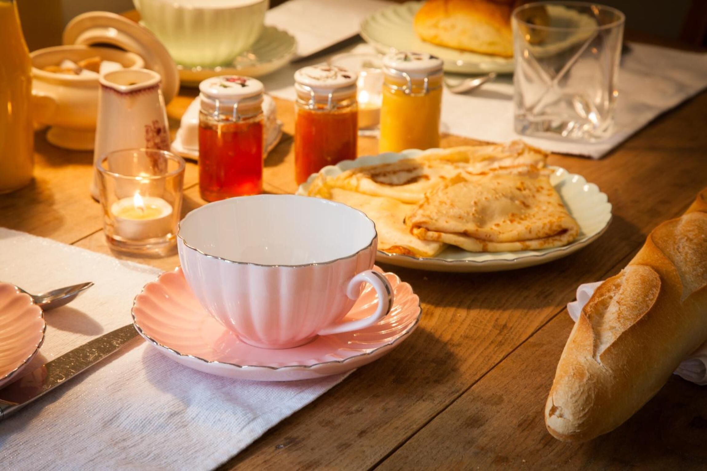 Een tafel met een roze beker, een bord eten, een glas en een pot jam.