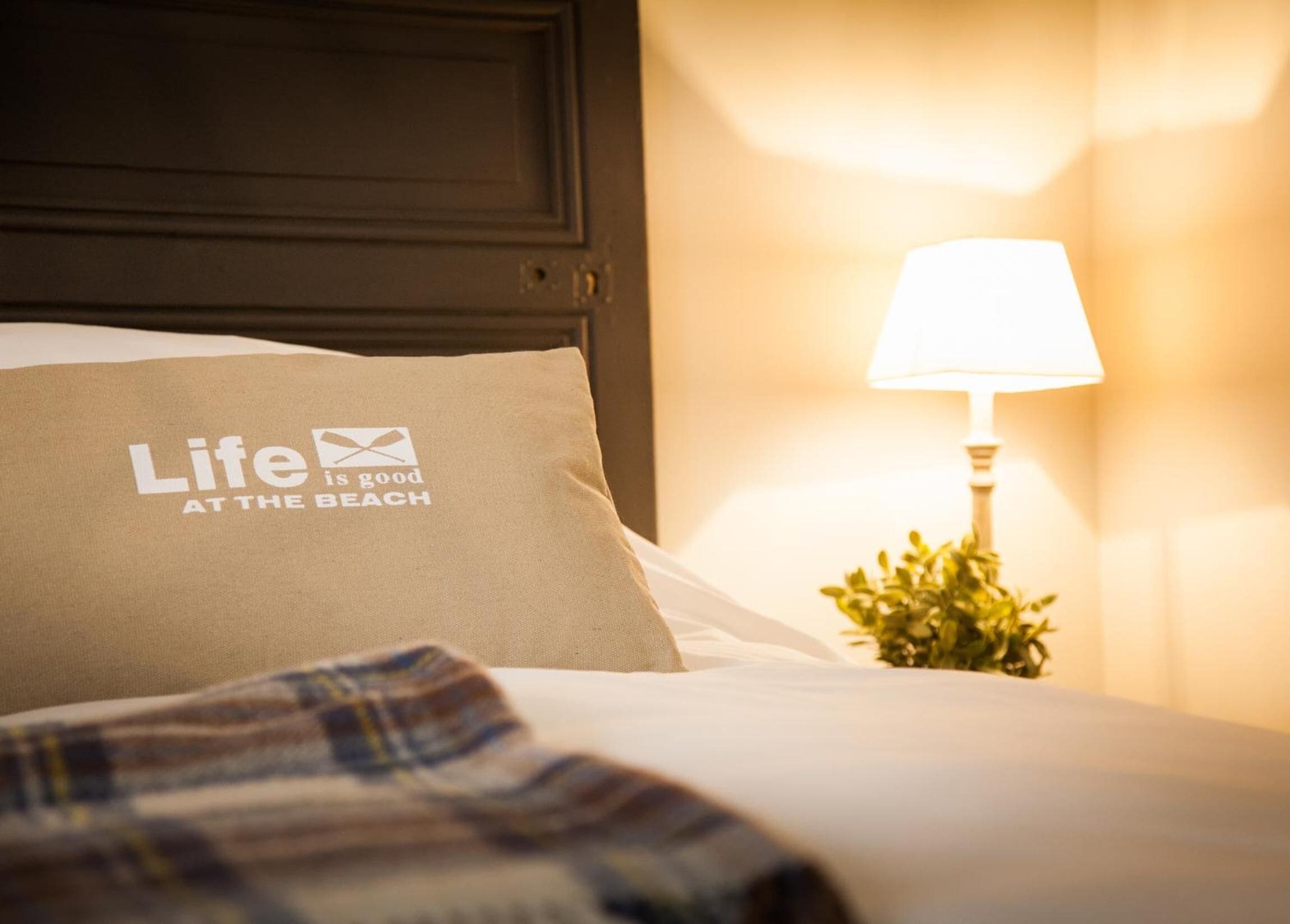 A hotel room with a bed featuring a pillow with the text "Life is good at the beach".