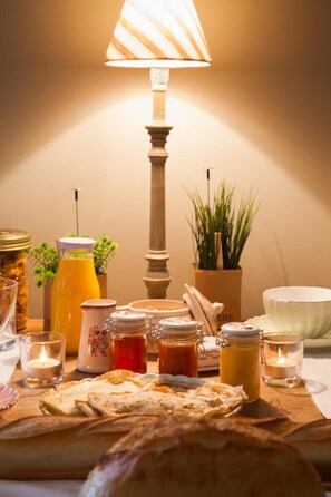 A breakfast table with various food items, a lamp, and candles. - Il était une fois chez moi Maison hôtes (Le Loroux-Bottereau)