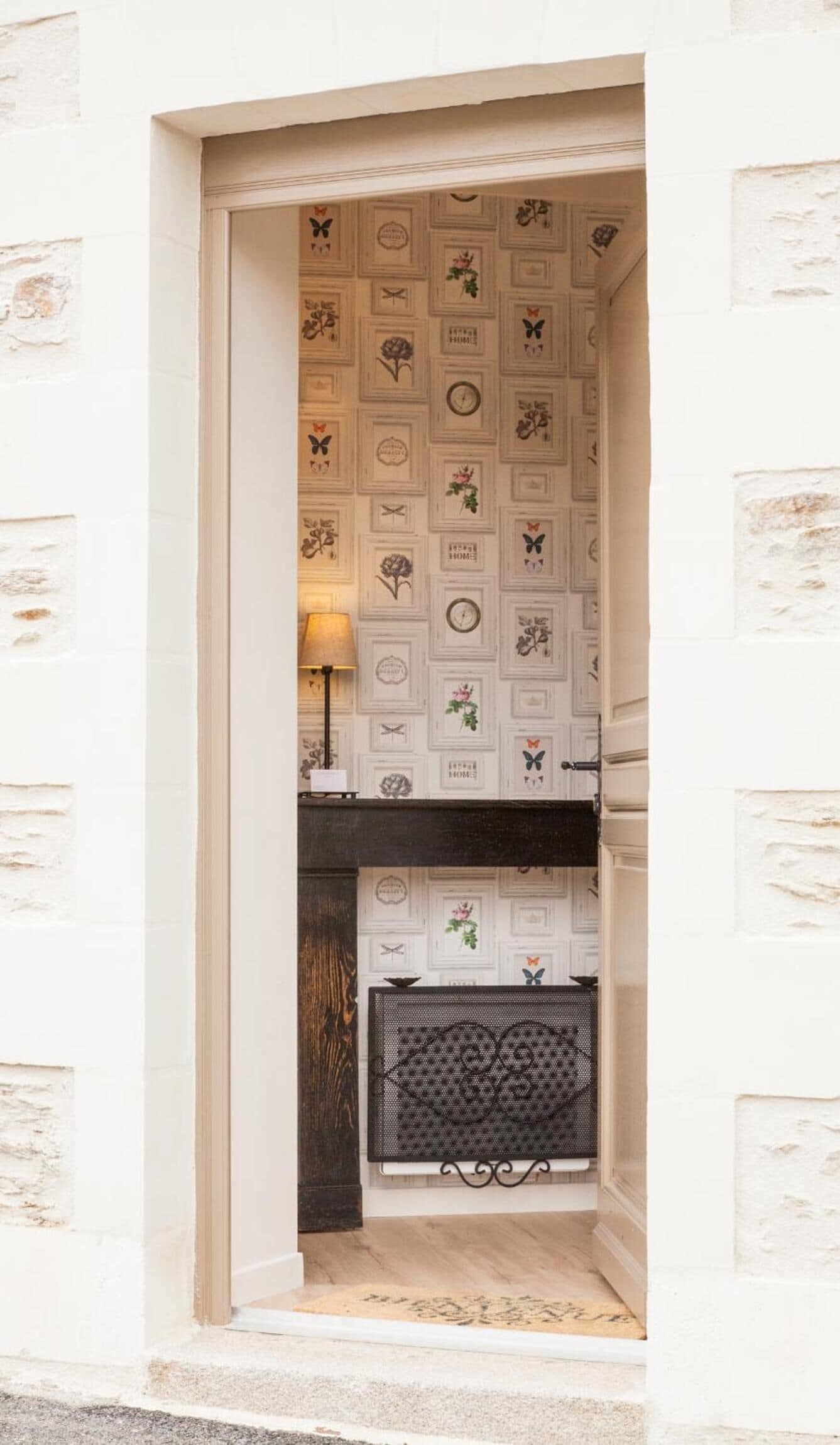 A narrow doorway with a patterned wall, a small table with a lamp, and a decorative fireplace.