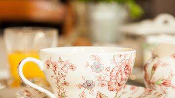A floral-patterned tea set with a cup and saucer, a glass of orange juice, and a candle in the background.
