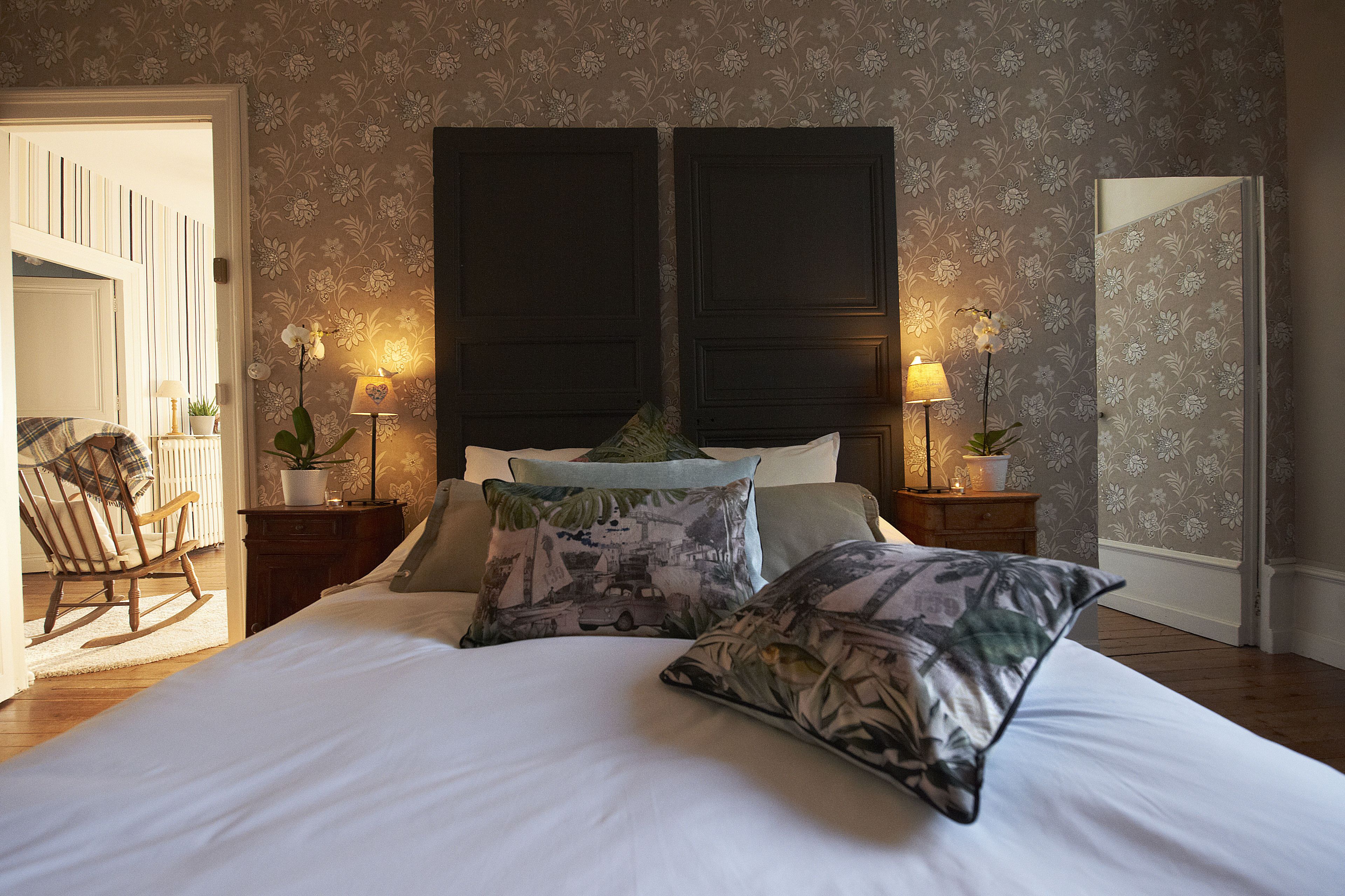 Una camera da letto con un letto grande, due comodini con lampade, una poltrona a dondolo e carta da parati floreale.