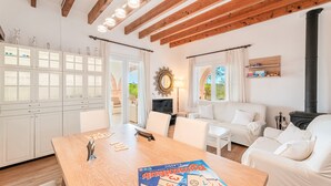 A modern interior with a wooden ceiling, white furniture, a dining table with a board game, and a fireplace. - Villa Rosa – Cala Mondragó (Santanyí)