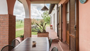 Eine Terrasse im Freien mit Tisch, Stühlen, einer hängenden Lampe und Blick auf einen Garten.
