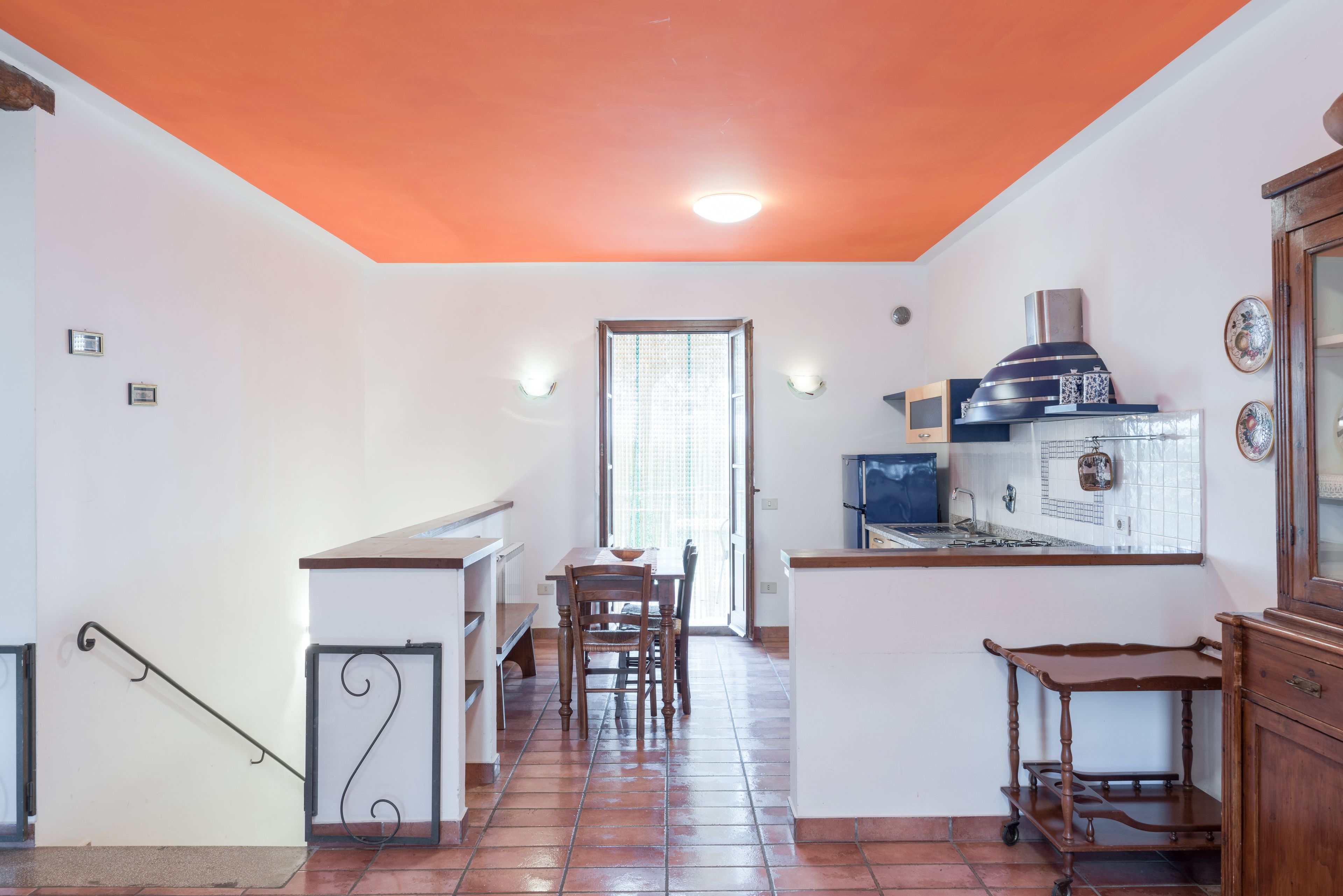 A kitchen with a tiled floor, a dining table with chairs, a small refrigerator, and a stove.