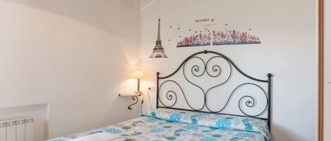 A bedroom with a bed, a wall-mounted lamp, and a poster of the Eiffel Tower.