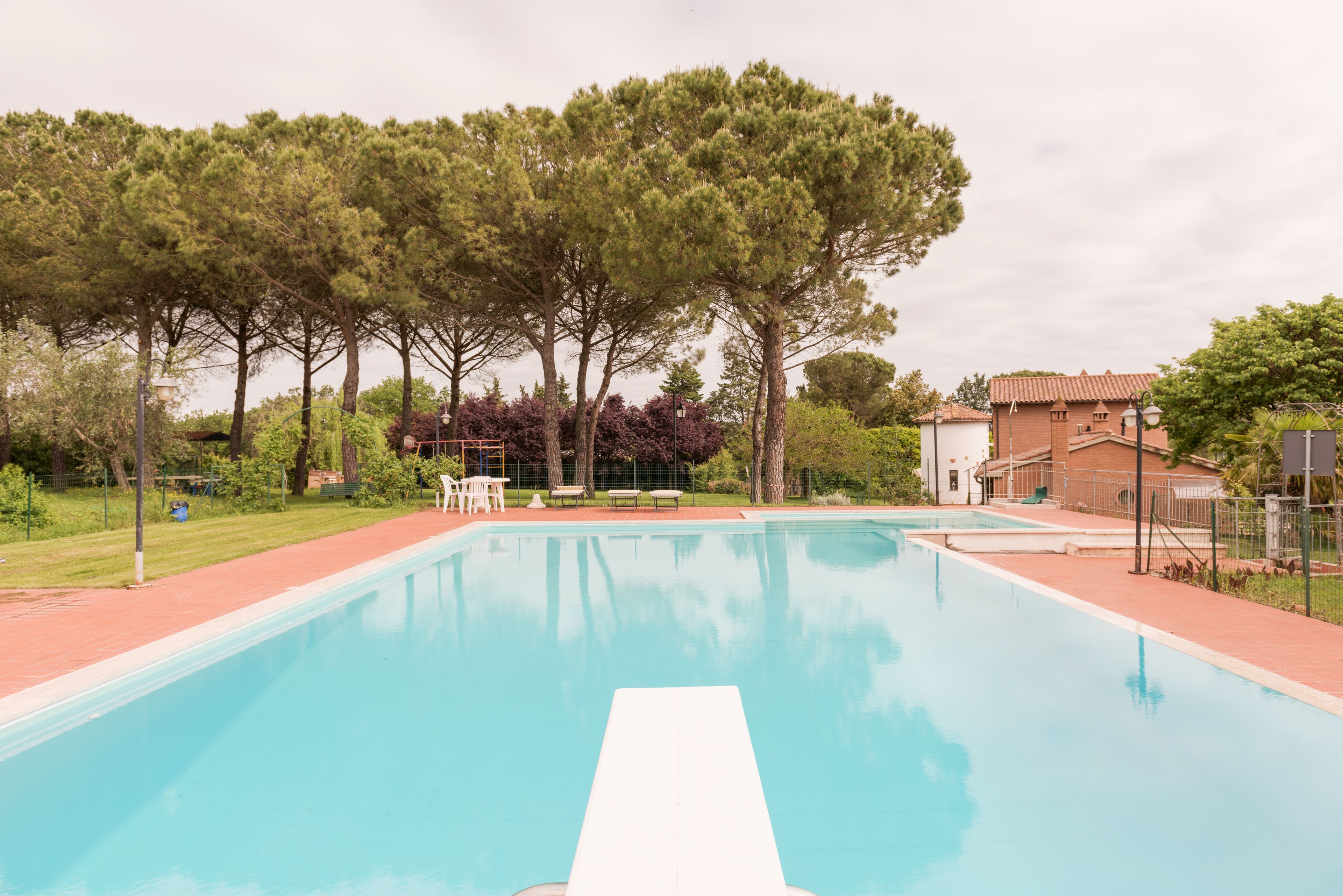 A rectangular swimming pool with a white diving board in the center, surrounded by a brick deck.
