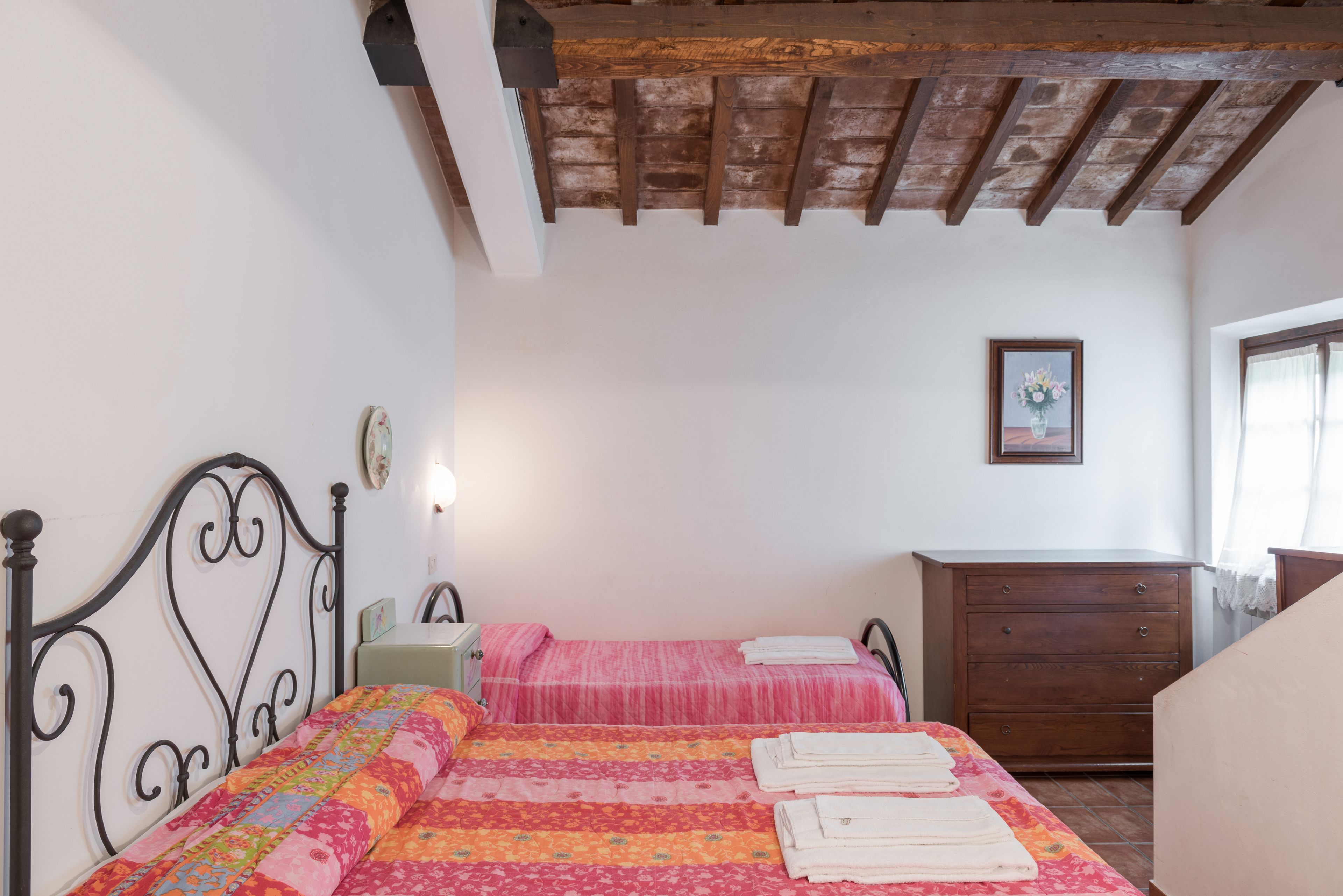 A bedroom with two beds, a wooden dresser, and a framed picture on the wall.